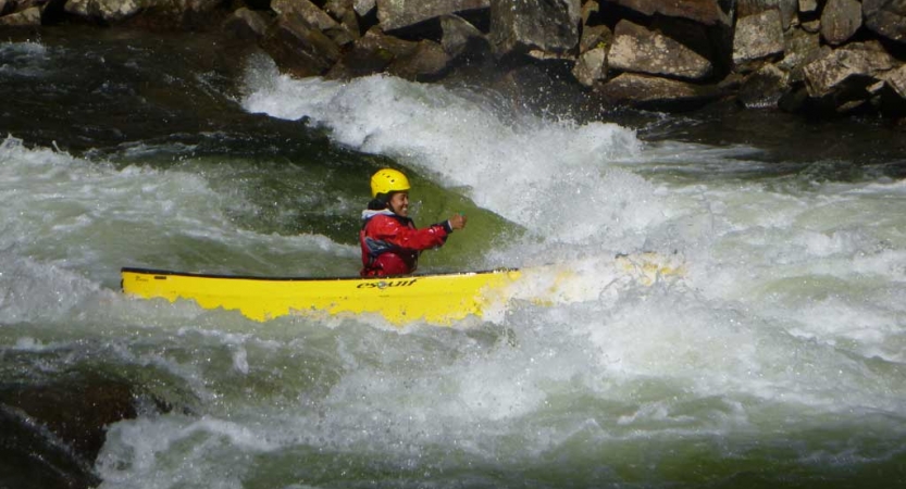A person wearing safety gear paddles a yellow canoe through rapids. 